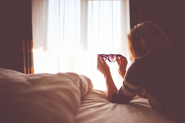 Žena, ktorá drží slnečné okuliare v rukách a leží na posteli.jpg