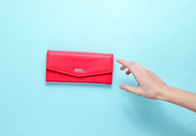 minimalism-trend-female-hand-takes-red-leather-wallet-blue-background-top-view_175682-3136